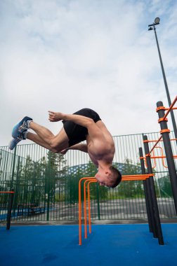 Açık hava spor sahasında ters takla atan genç bir erkek sporcu. Dikey fotoğraf