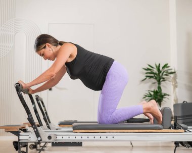 Hamile bir kadın yenilikçi bir makinede kalas kullanıyor. Perinatal yoga.