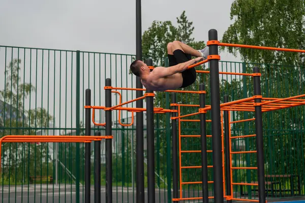 stock image A shirtless man is doing a workout on the horizontal bars outdoors