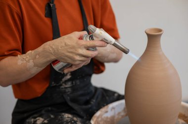 Çömlekçi ellerinin çömlekçi çarkında gaz ocağıyla sürahi ateşlediği yakın plan.