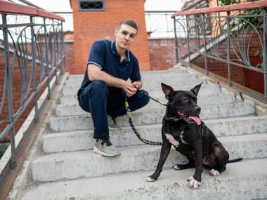 Merdivenlerde pitbull köpeği olan beyaz bir adam oturuyor.