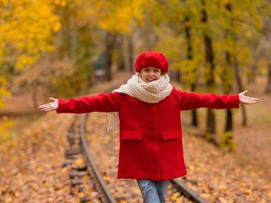 Kırmızılı ve bereli beyaz kız sonbaharda parkta tren yolu boyunca yürür.