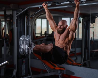 Kafkasyalı adam yatay çubuğa asılır ve bacaklarını kaldırır.