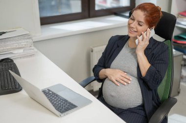 Ofiste cep telefonu kullanan hamile kadın.