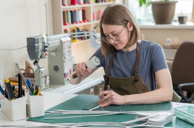 A woman makes holes in a leather belt in a workshop clipart