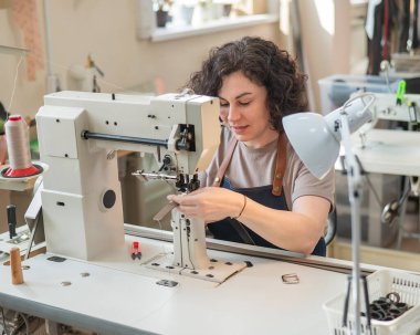 Bir kadın tabakçı dikiş makinesine deri kemer dikiyor.