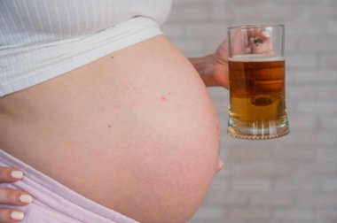 Elinde bira bardağıyla karnında isilik olan yüzü olmayan hamile bir kadın.