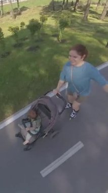 Beyaz kadın, oğluyla bebek arabasında paten kayıyor. Dikey video