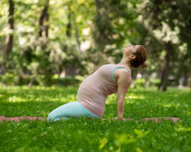 Parkta yoga yapan hamile, beyaz bir kadın. Geriye eğil