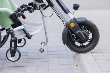 Tekerlekli sandalyedeki yüzü olmayan ve manuel kontrol için yardımcı bir aleti olan bir kadın. Elektrikli bisiklet.