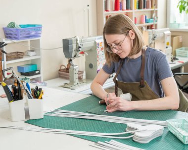 Bir kadın atölyede deri kemerde delikler açıyor.