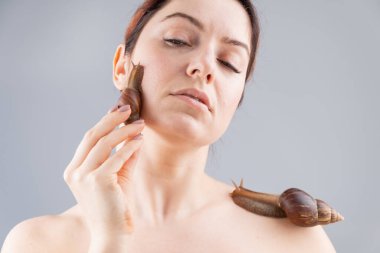 Yüzünde salyangozlar olan güzel beyaz bir kadın. Deri yenileme terapisi.