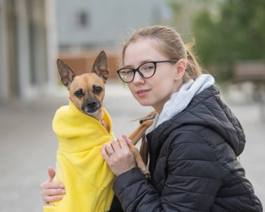 Beyaz bir kadının portresi. Ceketli küçük bir köpeğe sarılıyor.