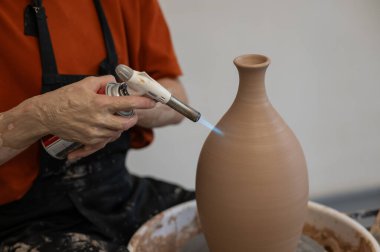 Çömlekçi ellerinin çömlekçi çarkında gaz ocağıyla sürahi ateşlediği yakın plan.