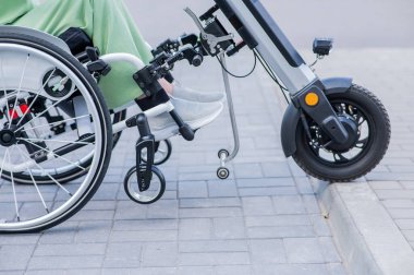 Tekerlekli sandalyedeki yüzü olmayan ve manuel kontrol için yardımcı bir aleti olan bir kadın. Elektrikli bisiklet.