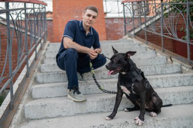 Merdivenlerde pitbull köpeği olan beyaz bir adam oturuyor.