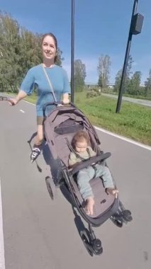 Beyaz kadın, oğluyla bebek arabasında paten kayıyor. Dikey video