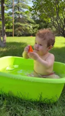 Şirin bir bebek plastik bir havuzda banyo yapar ve yazın dışarıda bir oyuncakla oynar. Dikey video