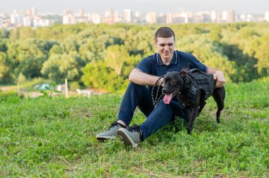 Kafkasyalı adam yeşil çimlerde pitbull teriyeriyle oturuyor.