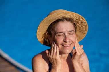 Tatildeyken yüzüne güneş kremi süren yaşlı bir kadının portresi.