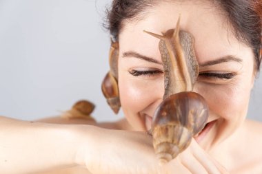 Büyük bir salyangoz tutan beyaz bir kadının yakın çekimi. Kozmetolojide kabuklu deniz hayvanı kullanımı