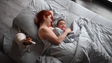 Kızıl saçlı beyaz bir kadının bebek oğlu ve Jack Russell terrier köpeğiyle yatakta yatışının en güzel görüntüsü.