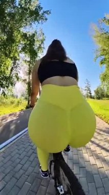 Büyük kalçalı beyaz bir kadının parlak tozluklarla bisiklet sürüşünün arka görüntüsü.
