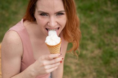 Genç, güzel, kızıl saçlı, diş telleriyle gülümseyen ve dışarıda dondurma yiyen bir kadın.