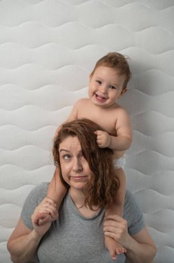 Top view of a sleepy mother and a little cheerful boy lying in bed. Vertical photo clipart