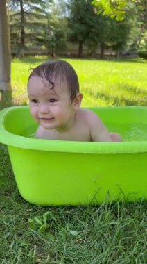 Şirin bir bebek plastik bir havuzda banyo yapar ve yazın dışarıda bir oyuncakla oynar. Dikey video