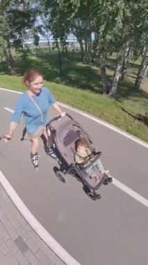 Beyaz kadın, oğluyla bebek arabasında paten kayıyor. Dikey video