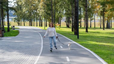 Beyaz kadın, Jack Russell Terrier köpeğiyle parkta paten kayıyor.