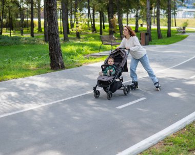 Beyaz kadın bebek arabasıyla küçük oğluyla paten kayıyor.