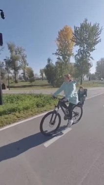 Beyaz bir kadın parkta yeni yürümeye başlayan oğluyla bisiklet sürüyor. Dikey video