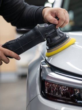 Yörüngesel cilalama makinesi kullanılarak beyaz arabanın kaput yüzeyinin parlatılması işlemi. Dikey fotoğraf