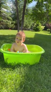 Şirin bir bebek plastik bir havuzda banyo yapar ve yazın dışarıda bir oyuncakla oynar. Dikey video