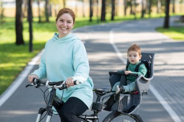 Küçük oğluyla bisiklete binen beyaz bir kadın arkasında çocuk koltuğunda oturuyor.