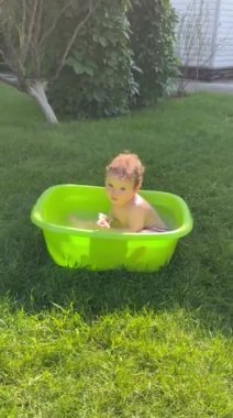 Şirin bir bebek plastik bir havuzda banyo yapar ve yazın dışarıda bir oyuncakla oynar. Dikey video