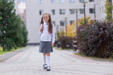 Beyaz üniformalı ve sırt çantalı bir kız okuldan ayrılıyor.