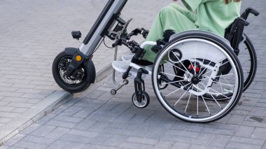 Tekerlekli sandalyedeki yüzü olmayan ve manuel kontrol için yardımcı bir aleti olan bir kadın. Elektrikli bisiklet.