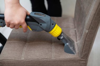 Kadın, elektrikli süpürgeyle kumaş sandalyesini temizliyor.