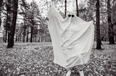 Bir sonbahar ormanının arka planında hayalet kostümlü bir kadın. Cadılar Bayramı kostümü. Siyah beyaz fotoğraf