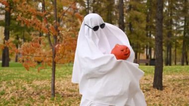 Beyaz çarşaflı kadın, sonbahar ormanlarında Jack Olantern 'ı tutuyor. Cadılar Bayramı kostümü