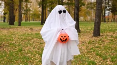 Beyaz çarşaflı bir kadın elinde balkabağı şeklinde bir sepet tutuyor ve sonbahar ormanından şeker istiyor. Cadılar Bayramı kostümü