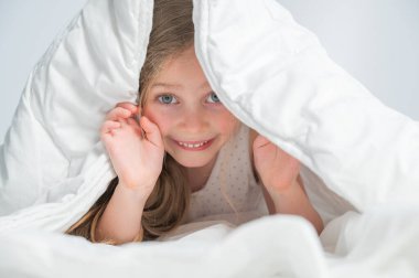 Küçük şirin bir kızın portresi. Battaniyenin altında gülüyor ve saklanıyor.