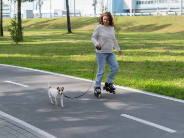 Beyaz kadın, Jack Russell Terrier köpeğiyle parkta paten kayıyor.