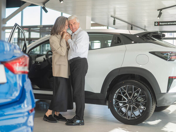 Зрелая белая пара обнимается со счастьем, покупая новую машину