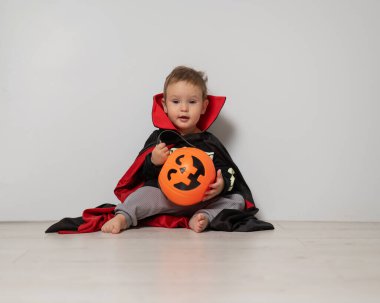 Beyaz arka planda şeker sepeti tutan Drakula kostümlü beyaz çocuk. Şaka mı şeker mi?