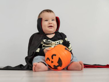 Beyaz arka planda şeker sepeti tutan Dracula Cadılar Bayramı kostümlü beyaz tatlı çocuk.