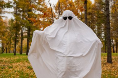 Bir sonbahar ormanının arka planında hayalet kostümlü bir kadın. Cadılar Bayramı kostümü